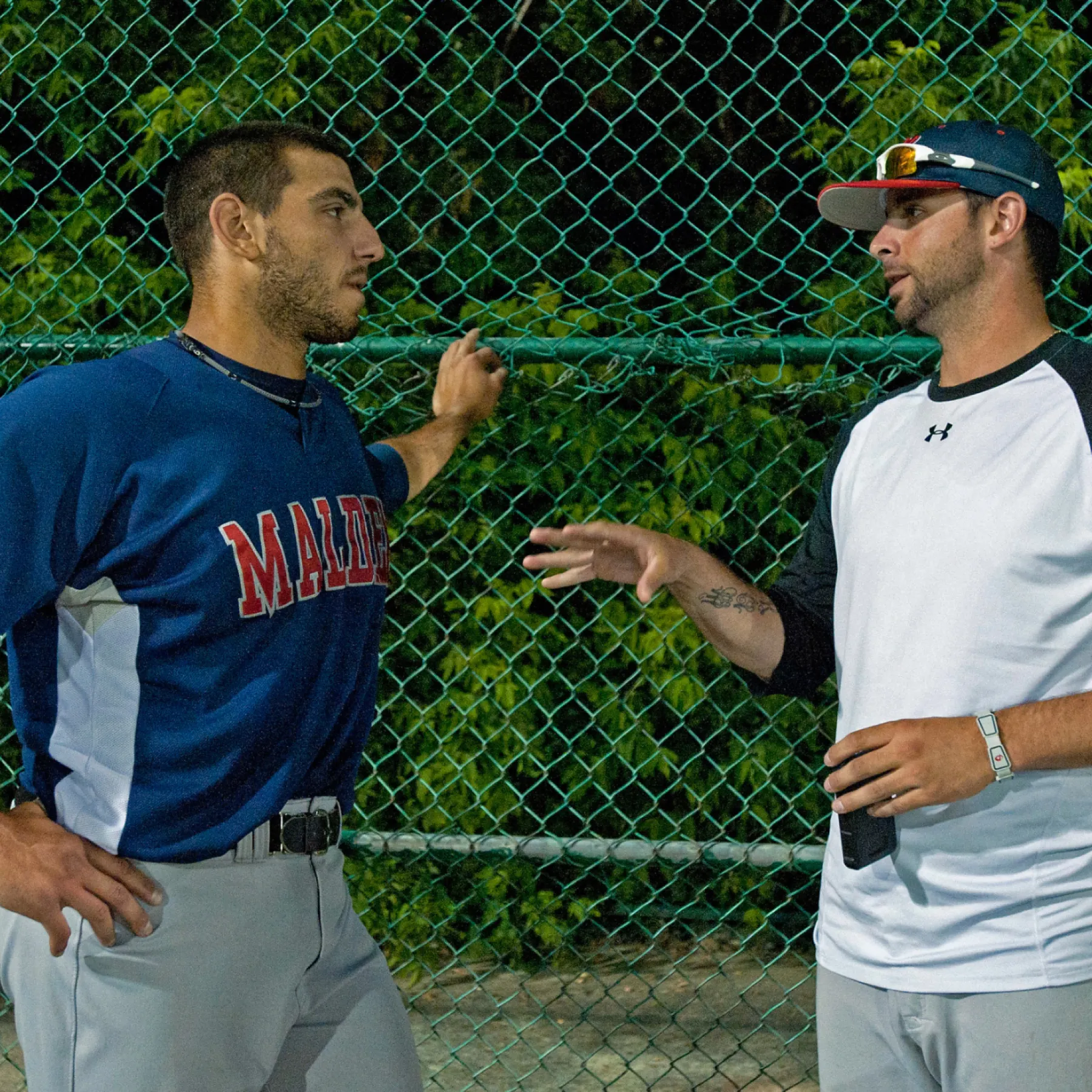 Coach Jeff Allison talking with a ballplayer beside the fence during an evening workout
